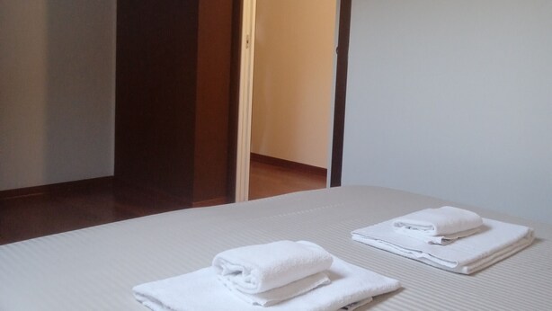 A hotel room with a bed, two neatly folded white towels, and a wooden door leading to another room. - Business and vacation in an 'oasis of peace!!! (Valdarenne)