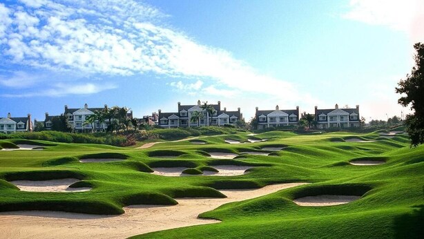 A golf course with bunkers and a clubhouse in the background.