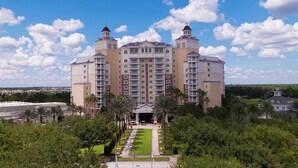 A large, multi-story hotel with a central courtyard, surrounded by lush greenery and palm trees.