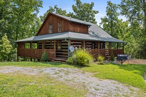A rustic log cabin with a porch, surrounded by lush greenery. - Boho Chic Cabin: Hot Tub - Mountain View’s - FREE Early Checkin- May DEALS (Sevierville)