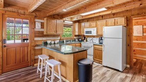 Cocina de cabaña de madera con una isla central, taburetes de barra blancos, un refrigerador blanco y armarios de madera.