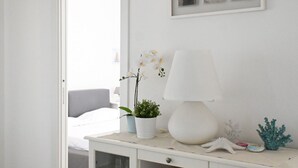 Un dormitorio con una cama, una mesita de noche con lámpara, una planta en maceta y elementos decorativos.