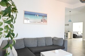 A modern living room with a grey sectional sofa, a white coffee table, a framed picture of a beach scene, and a hanging plant. - S270 - Sirolo, four-room apartment in the center with a panoramic view (Sirolo)