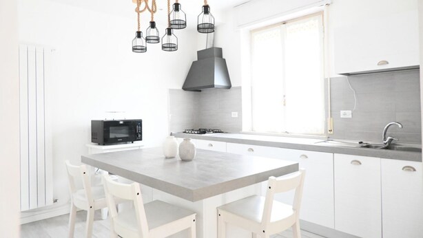 Una cocina moderna con una isla central, armarios blancos, microondas y cocina a gas.