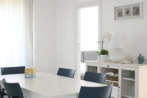 A white dining table with chairs, a white cabinet with shelves, and a window with curtains. - S270 - Sirolo, four-room apartment in the center with a panoramic view (Sirolo)