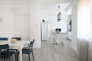 Une cuisine moderne avec des meubles blancs, un coin repas doté d’une table blanche et de chaises bleues, et un luminaire suspendu.