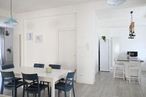 A modern kitchen with white cabinetry, a microwave, and a dining area with a white table and blue chairs.