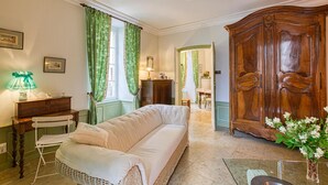 Ein gemütliches Zimmer mit einer Couch, einem Holzschrank, einer Lampe und einem Essbereich, der durch eine offene Tür sichtbar ist.