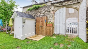 Ein kleiner weißer Schuppen mit Holztür, Steinmauer und hölzernem Tor.