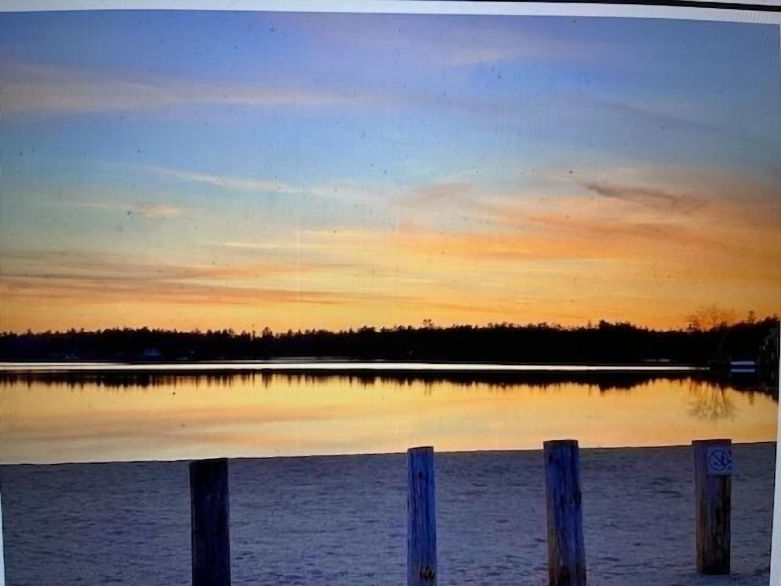 A calm lake at sunset with a wooden dock in the foreground.