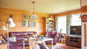 Een gezellige woonkamer met houten wanden, een leren bank, een salontafel, een boekenkast, een televisie en een vloerkleed.