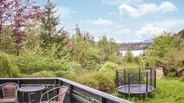 Een terras met rieten stoelen en een tafel, met uitzicht op een meer en een bebost gebied.