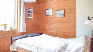 Een kamer met houten lambrisering, een bed, een raam met gordijnen en twee ingelijste foto's aan de muur.