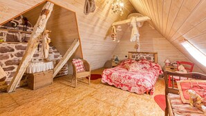 A cozy attic bedroom with a sloped ceiling, a bed with a floral bedspread, a wicker chair, and a small table with a lamp. - 2 bedroom nice home in Saint Laurent d'Olt (Saint Laurent d'Olt)