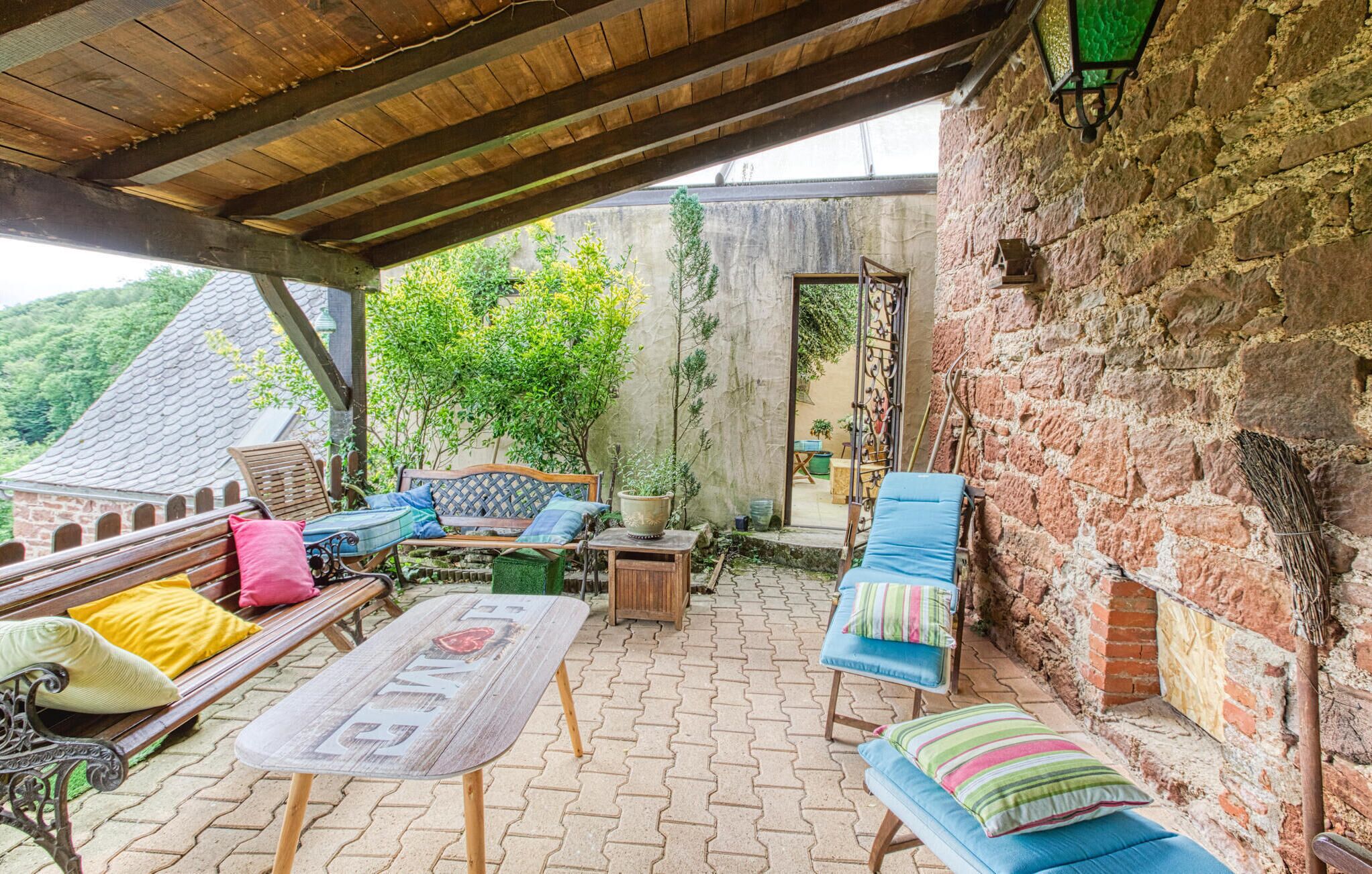 A covered outdoor seating area with wooden furniture, a table, and a brick wall.