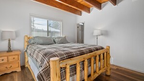 A bedroom with a wooden bed frame, a nightstand, a bedside lamp, and a window with blinds. - Game Cabin with 5 PM Late Checkout (Big Bear)