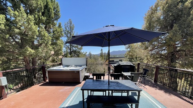 An outdoor patio with a hot tub, a table with chairs, and an umbrella. - Game Cabin with 5 PM Late Checkout (Big Bear)