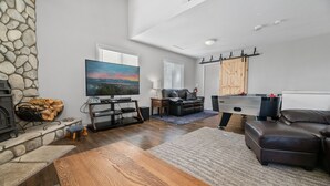 A living room with a stone fireplace, a flat-screen TV, a leather sofa, and a pool table. - Game Cabin with 5 PM Late Checkout (Big Bear)