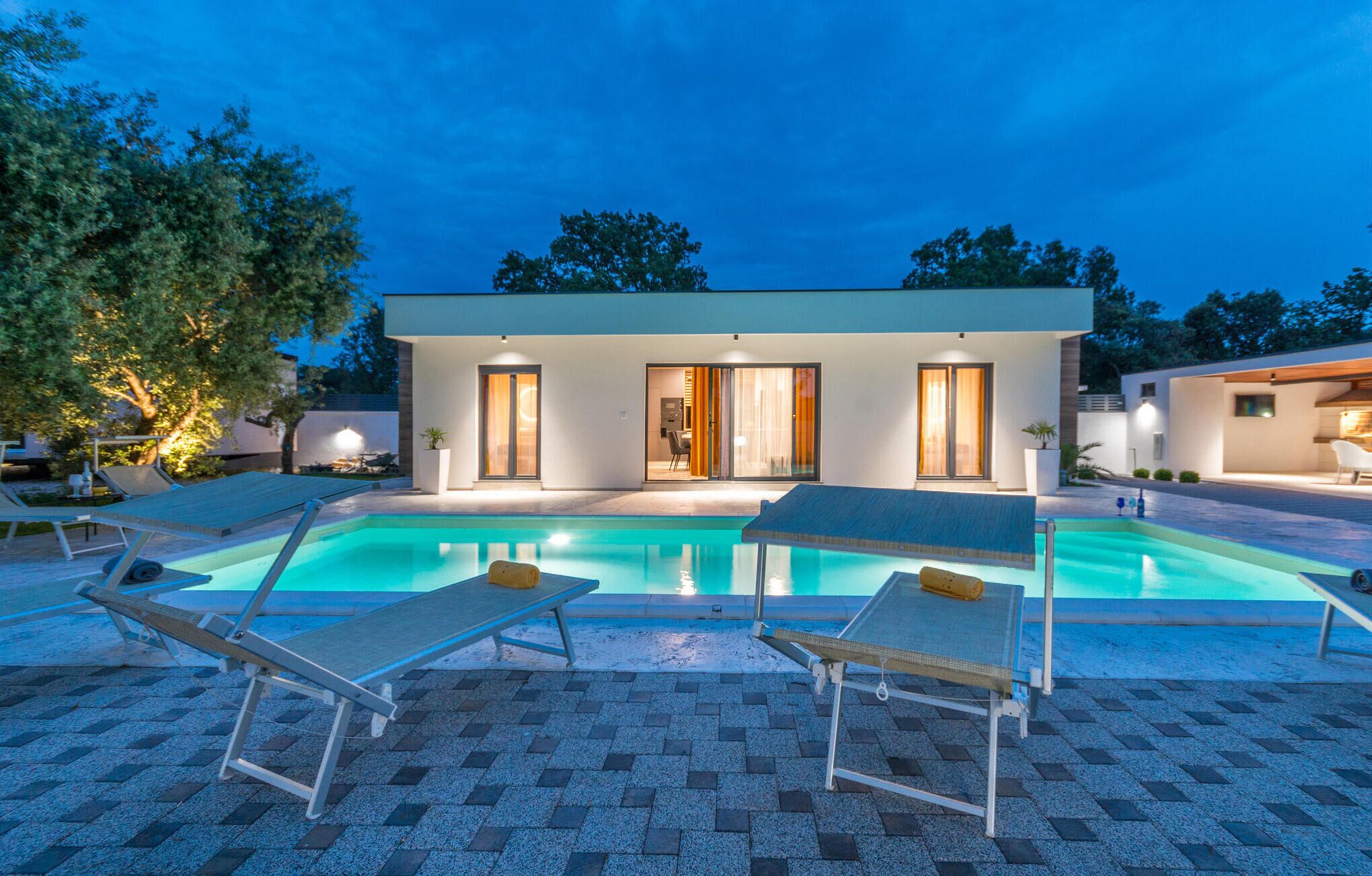 Uma casa moderna com piscina, duas portas e um pátio com espreguiçadeiras.