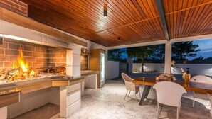 Una cocina exterior con chimenea de ladrillo, techo de madera y un comedor con sillas y mesa.