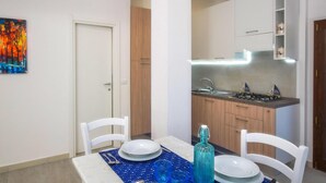 A dining area with a table set for four, a kitchen with modern appliances, and a colorful abstract painting on the wall. - 1 bedroom beach front home in Budoni (Budoni)