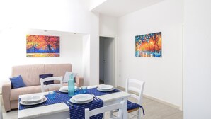 A dining area with a table set for four, a sofa, and two paintings on the walls. - 1 bedroom beach front home in Budoni (Budoni)