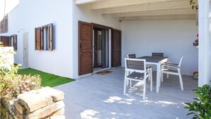 A patio with a table and chairs, a sliding glass door, and a small garden area with flowers. - 1 bedroom beach front home in Budoni (Budoni)