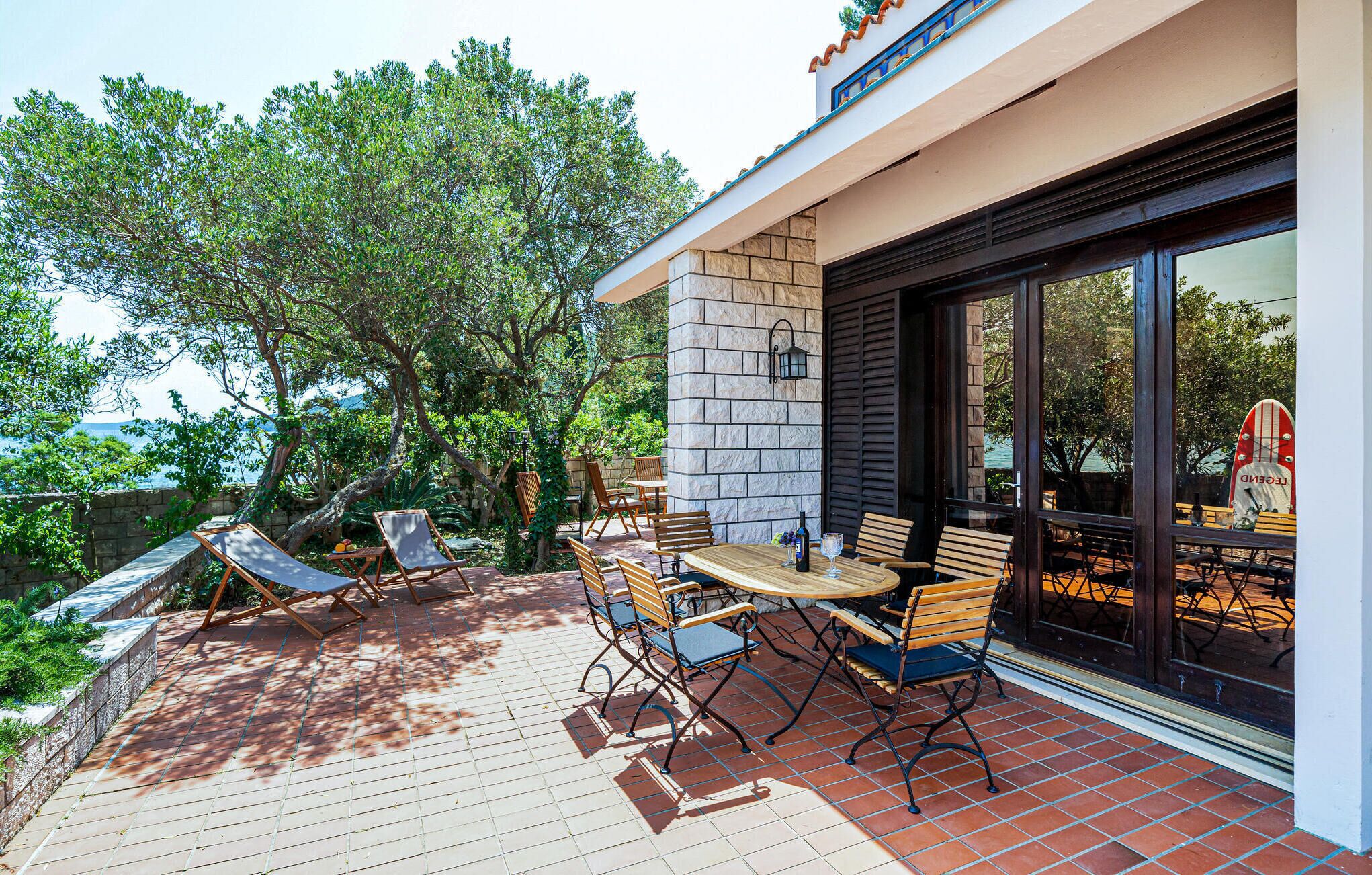 An outdoor patio with a stone wall, wooden furniture, and a view of the sea.