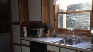 Eine kompakte Küche mit Holzausstattung, einer Mikrowelle, einem Spülbecken und einem Fenster mit Blick auf Bäume.