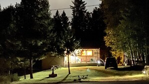 Eine Hütte mit Veranda, umgeben von Bäumen, und ein geparktes Auto in der Nähe.