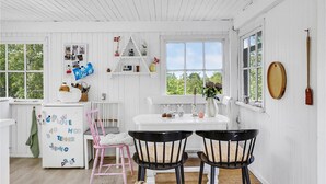 Un interior blanco con cocina, una mesa de comedor con dos sillas y un refrigerador decorado con imanes infantiles.
