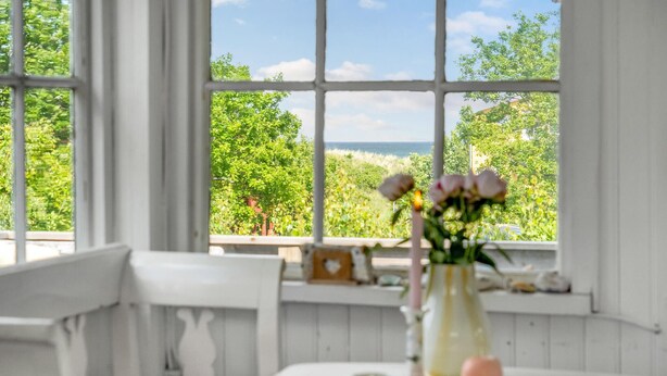 Una habitación con un ventanal que ofrece vistas a zonas verdes y un edificio. Un jarrón con flores está sobre una mesa.