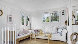 Una habitación de paredes blancas con un sofá de mimbre, una mesa de centro de madera y una silla de mimbre.