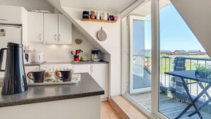 Une cuisine moderne avec des meubles blancs, un coin café et une vue sur une terrasse aménagée avec des sièges d’extérieur.