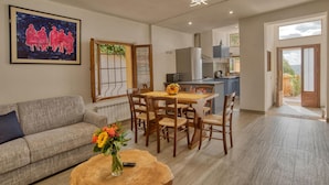 A living room with a sofa, a dining table with chairs, a vase with flowers, and a painting on the wall.