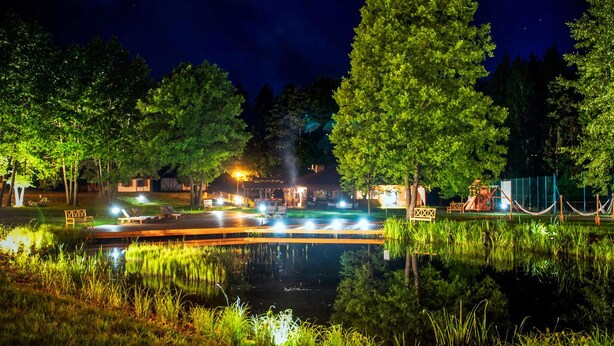 Un espacio al aire libre de noche con un estanque, árboles y un edificio iluminado.