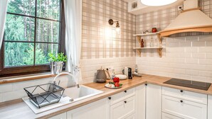 Cocina con armarios blancos, encimera de madera, un lavamanos, ventana con vistas a árboles y una lámpara colgante.