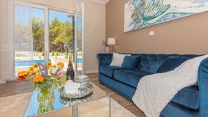 A living room with a blue sofa, a glass coffee table with flowers and a bottle, and a painting on the wall. - 3 bedroom gorgeous home in Jadrtovac (Jadrtovac)