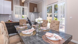 A dining area with a long table set for four, featuring a wine bottle, white flowers, and a candle. - 3 bedroom gorgeous home in Jadrtovac (Jadrtovac)