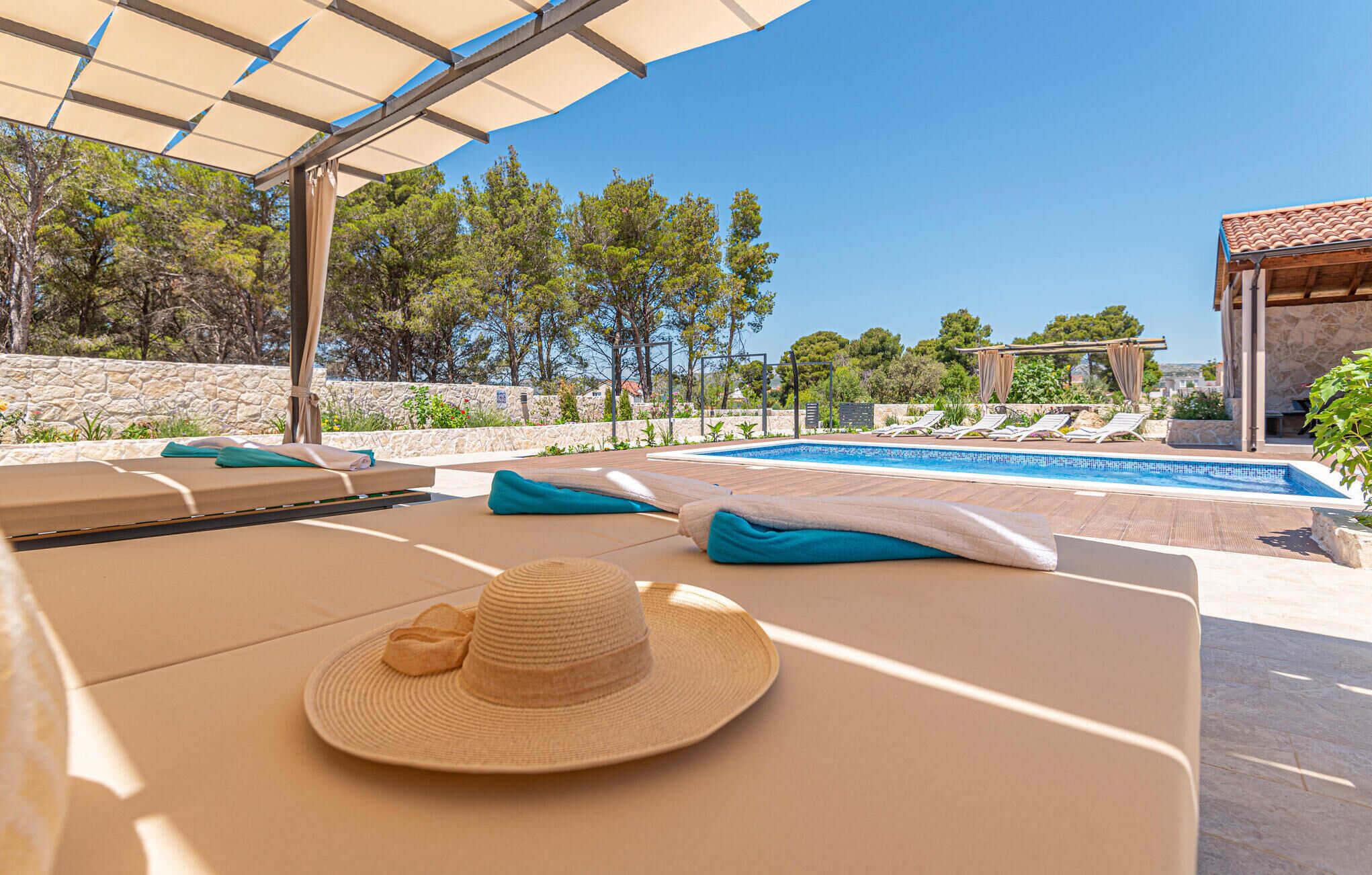 A poolside area with lounge chairs, a sun umbrella, and a hat on a towel.