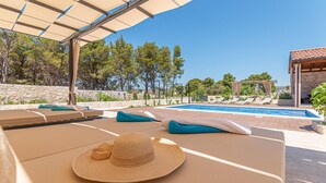 A poolside area with lounge chairs, a sun umbrella, and a hat on a towel. - 3 bedroom gorgeous home in Jadrtovac (Jadrtovac)