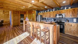 A wooden cabin interior with a central kitchen area featuring a bar, stools, and modern appliances. - 5 Decks | Hot Tub | Views | Fire Pit | Pool Table (Sevierville)