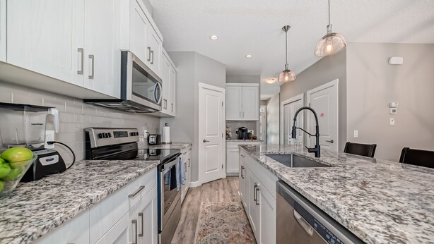 A modern kitchen with white cabinets, granite countertops, a stainless steel range hood, and pendant lighting. - Spacious Home w/ Sauna & Fenced Yard w/ BBQ, Pet-Friendly, Sleeps 10, King Beds (Calgary)
