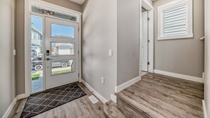 A modern entryway with a wooden floor, a glass door with a view of the outside, and a white wall with a window. - Spacious Home w/ Sauna & Fenced Yard w/ BBQ, Pet-Friendly, Sleeps 10, King Beds (Calgary)