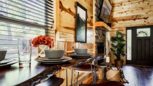 Un interior de madera con una mesa de comedor preparada para cuatro, una chimenea y una ventana con persianas.