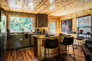 A rustic cabin interior with a kitchen, dining area, and bar stools.