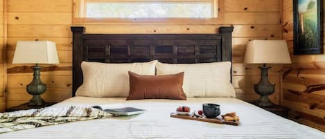 Ein Schlafzimmer einer Holzhütte mit einem großen Bett, zwei Nachttischlampen, einem Fenster und einem Gemälde an der Wand.