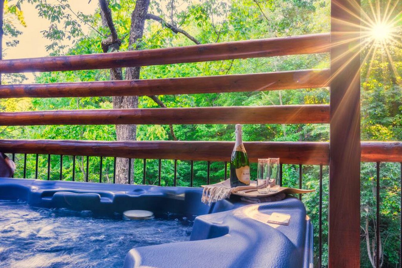 A hot tub with wooden railings and a bottle of champagne, surrounded by lush greenery.