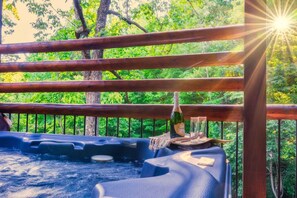 A hot tub with wooden railings and a bottle of champagne, surrounded by lush greenery.