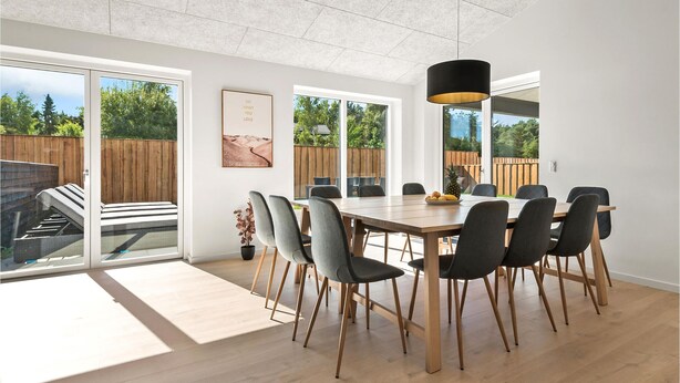 Un comedor moderno con una mesa y sillas de madera, ventanas amplias y vistas al jardín.